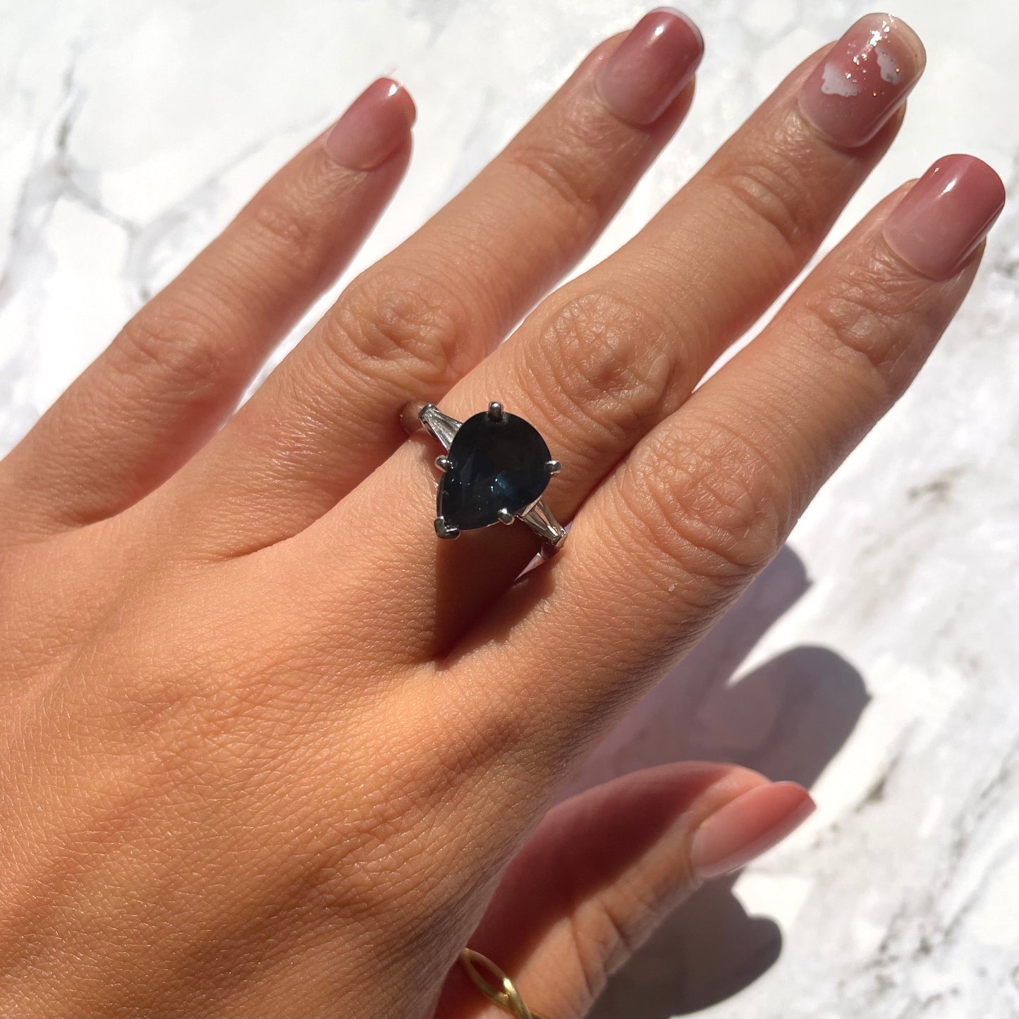 a hand wearing deep blue sapphire ring with 14k white gold band and natural white diamonds