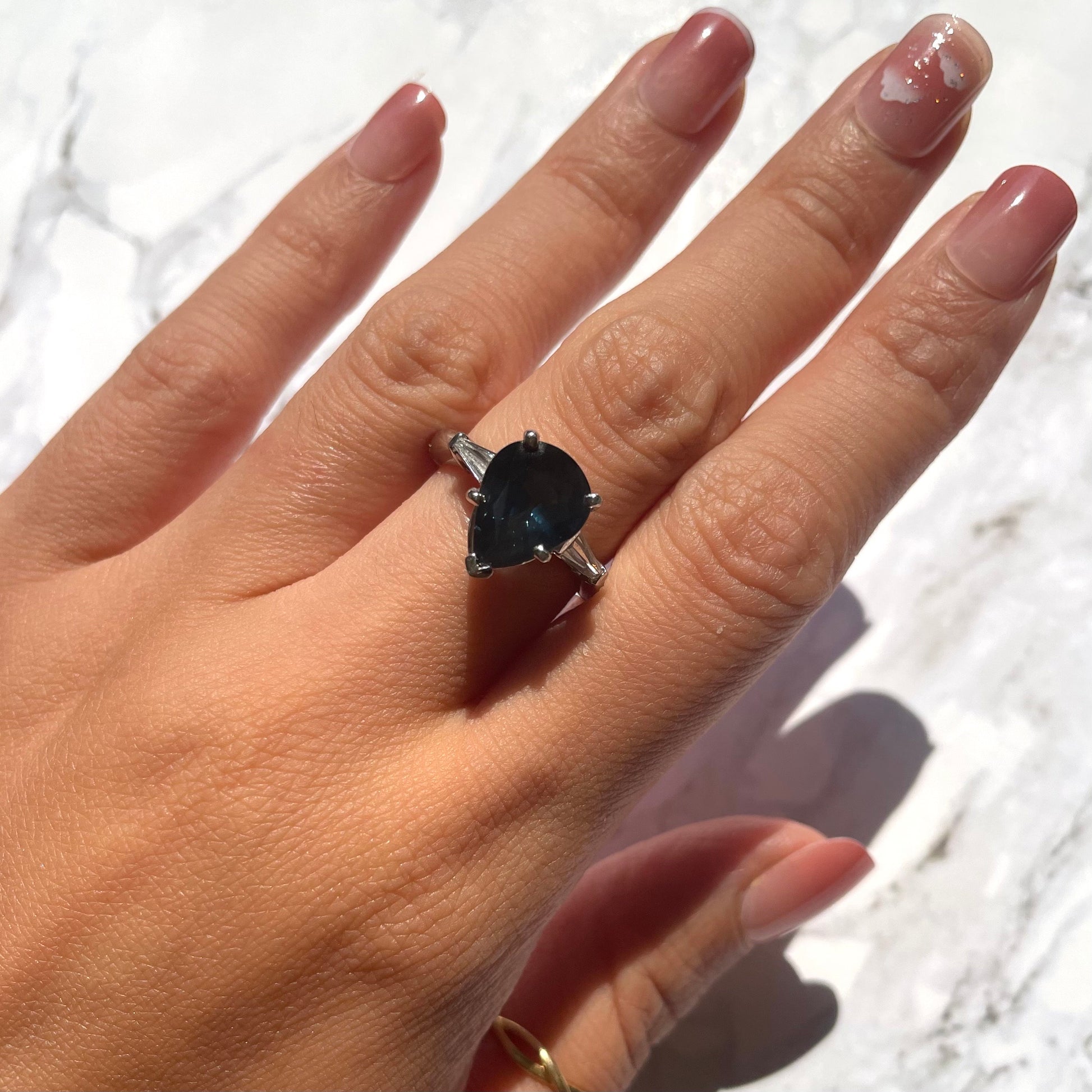 a hand wearing deep blue sapphire ring with 14k white gold band and natural white diamonds