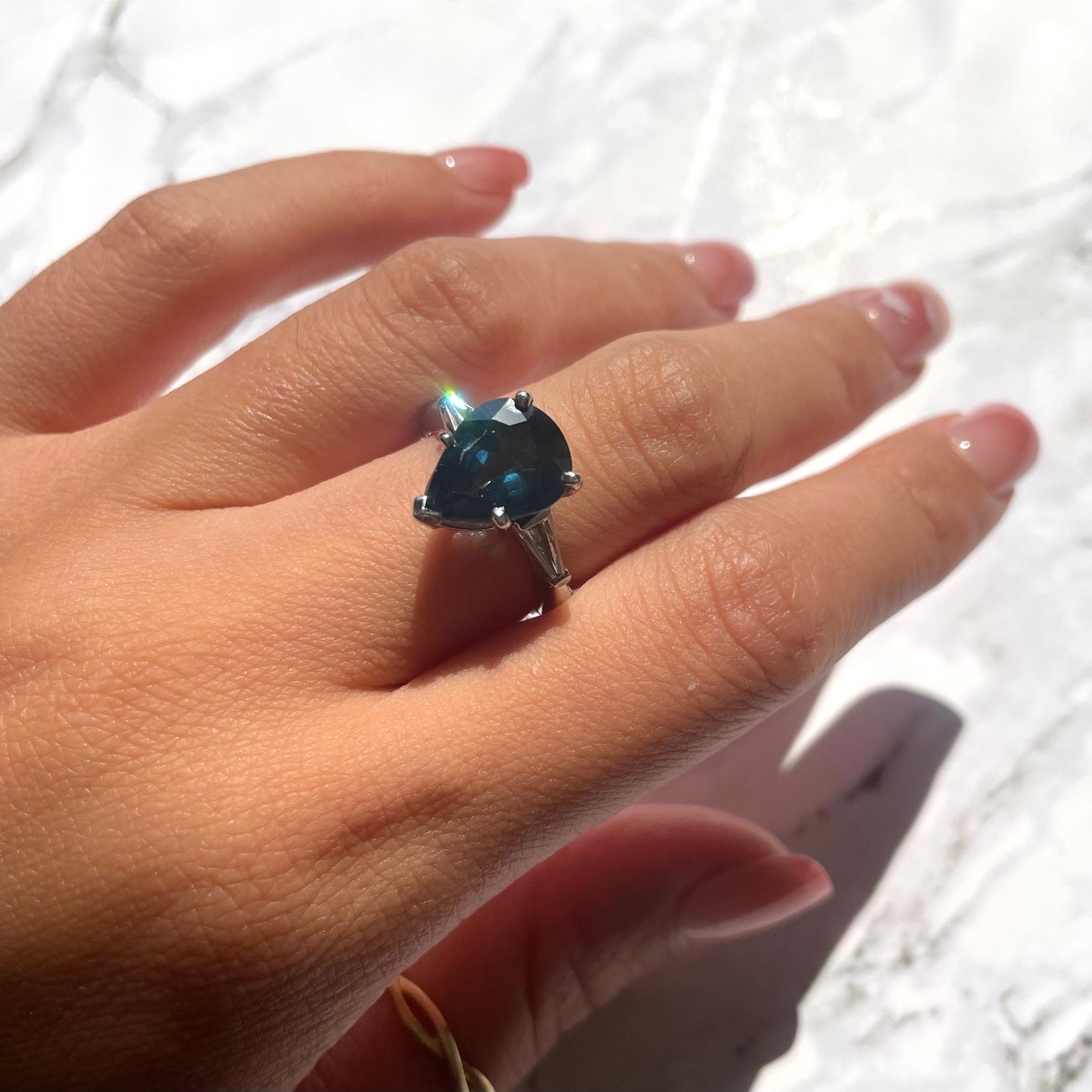 a hand wearing deep blue sapphire ring with 14k white gold band and natural white diamonds