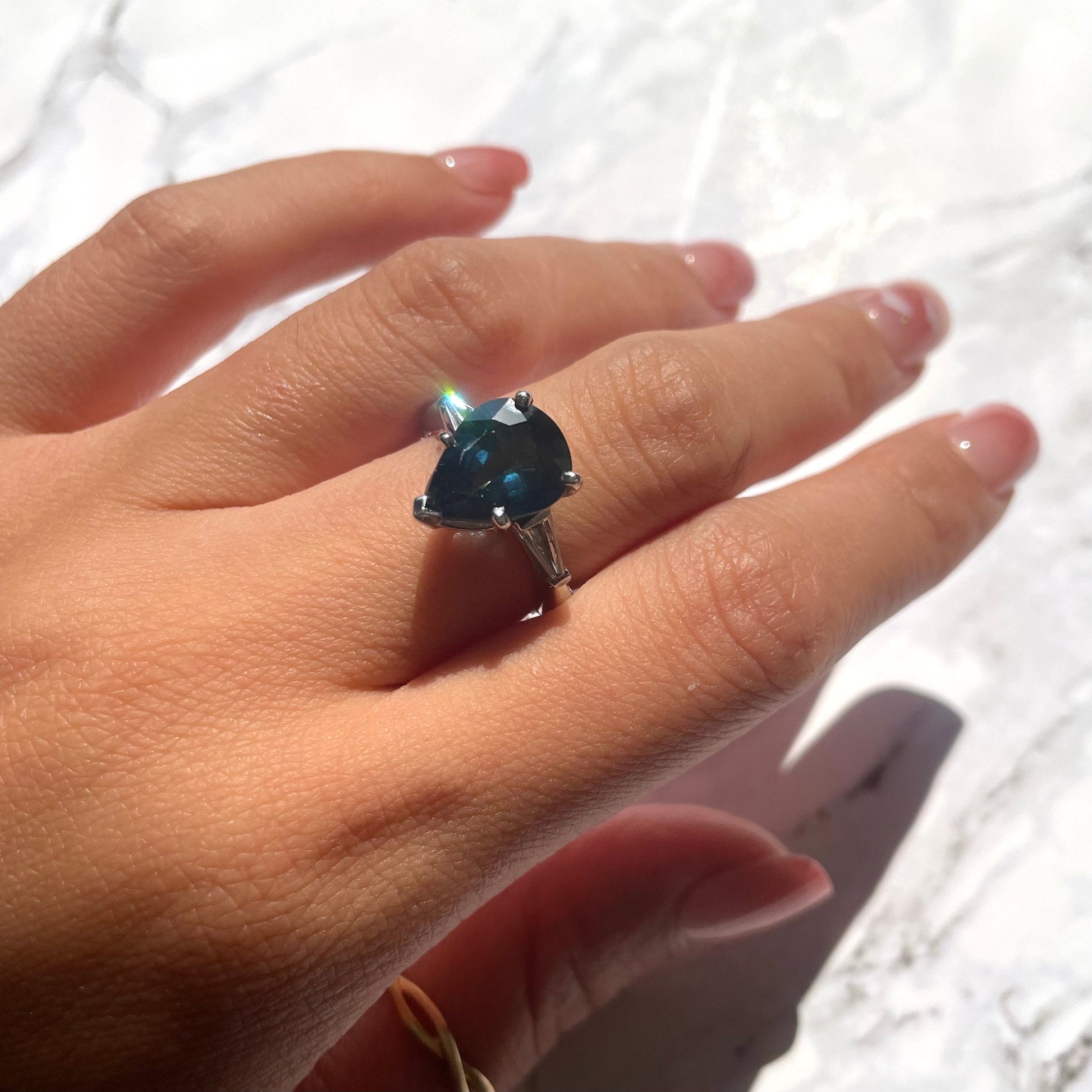 a hand wearing deep blue sapphire ring with 14k white gold band and natural white diamonds