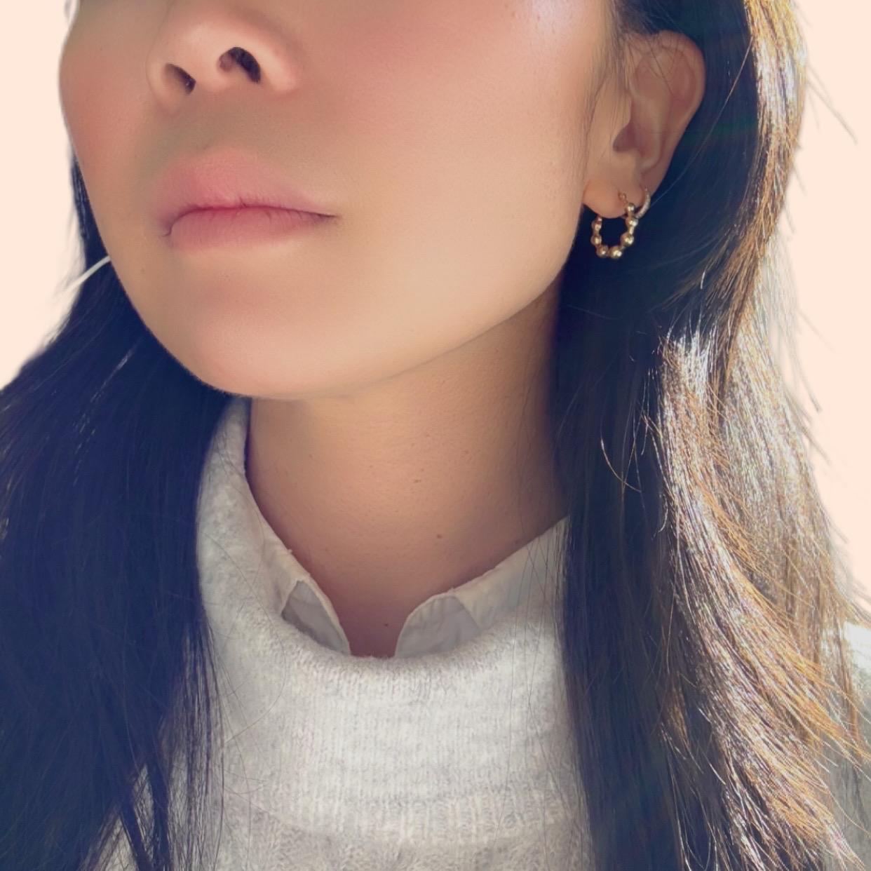 a girl wearing 14k solid gold beaded huggies hoop earrings with grey sweater and white shirt