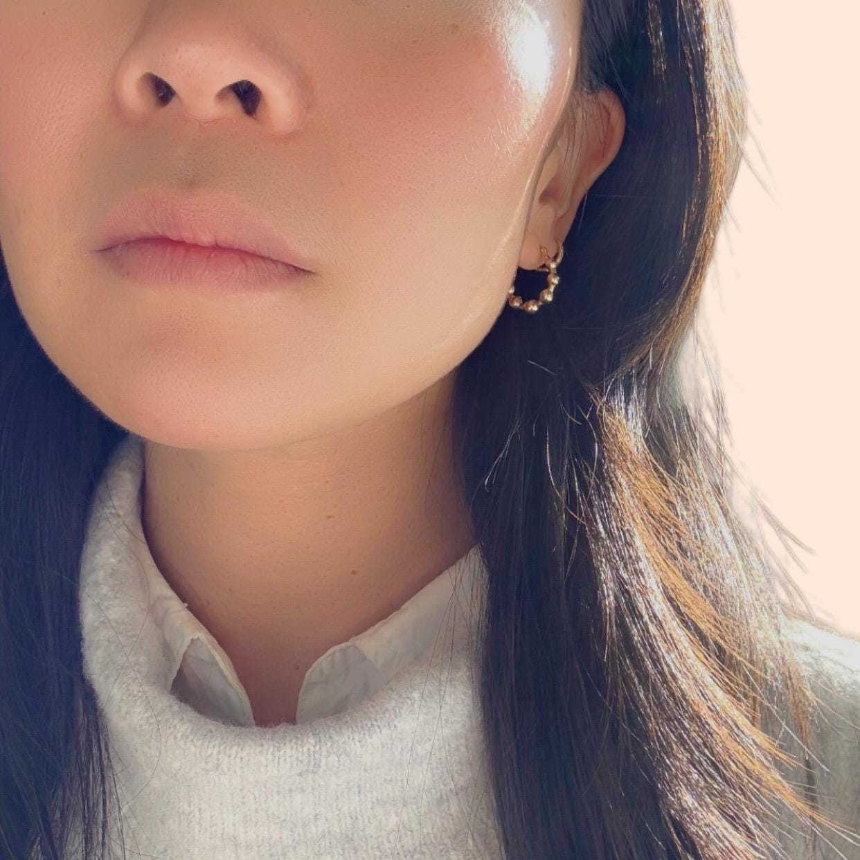 a girl wearing 14k solid gold beaded huggies hoop earrings with grey sweater and white shirt