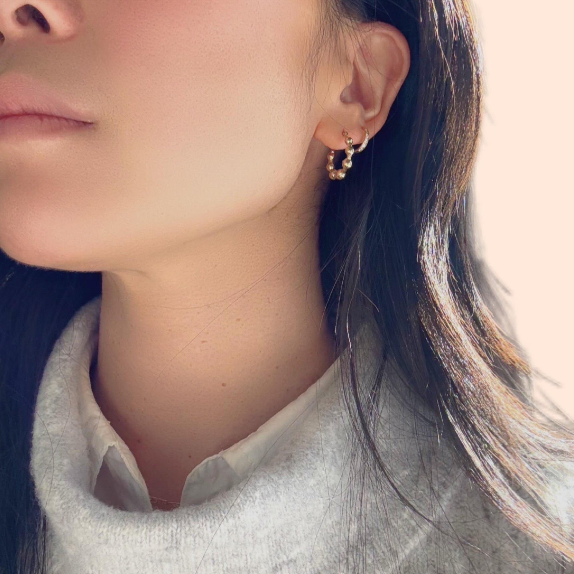 a girl wearing 14k solid gold beaded huggies hoop earrings with grey sweater and white shirt