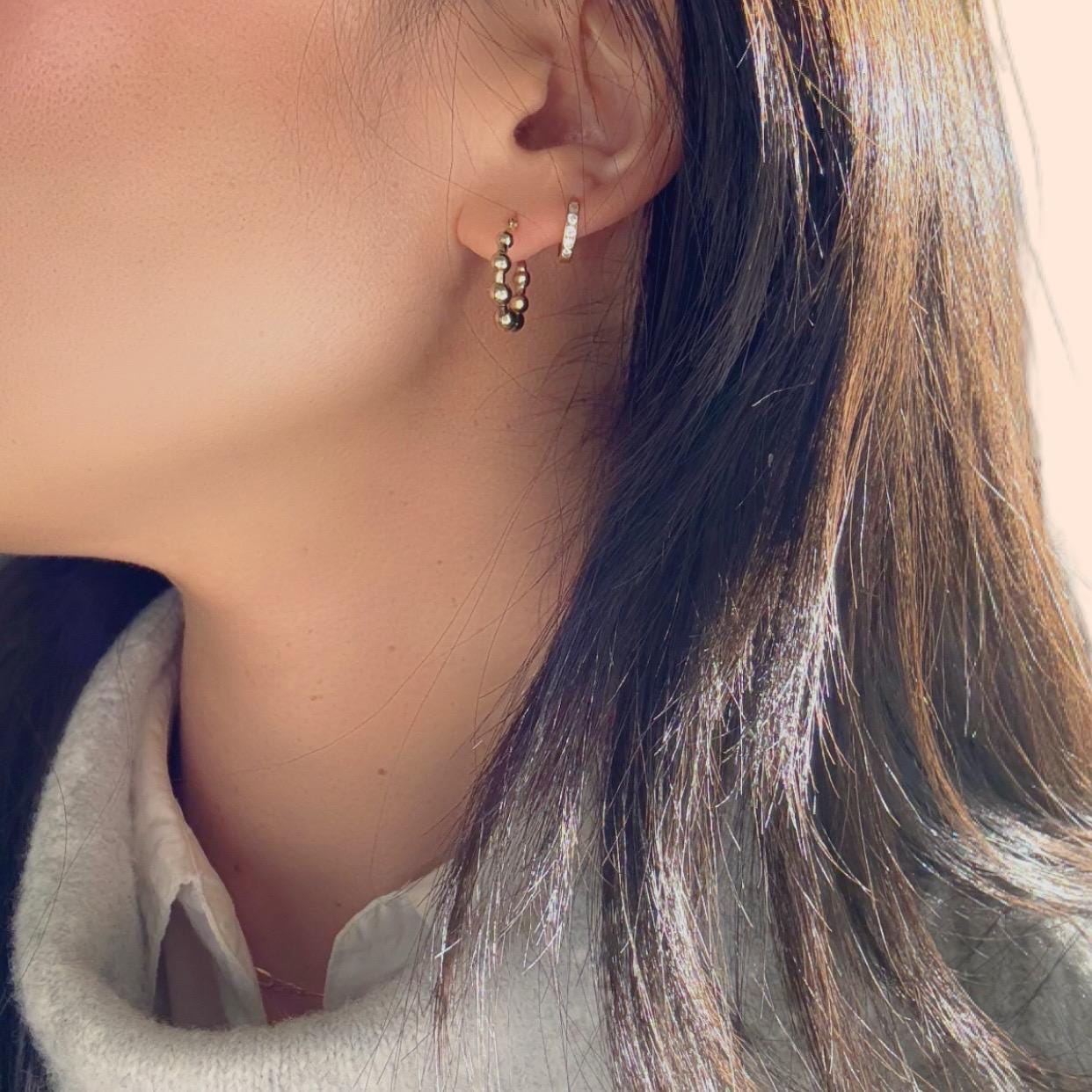 a girl wearing 14k solid gold beaded huggies hoop earrings with grey sweater and white shirt