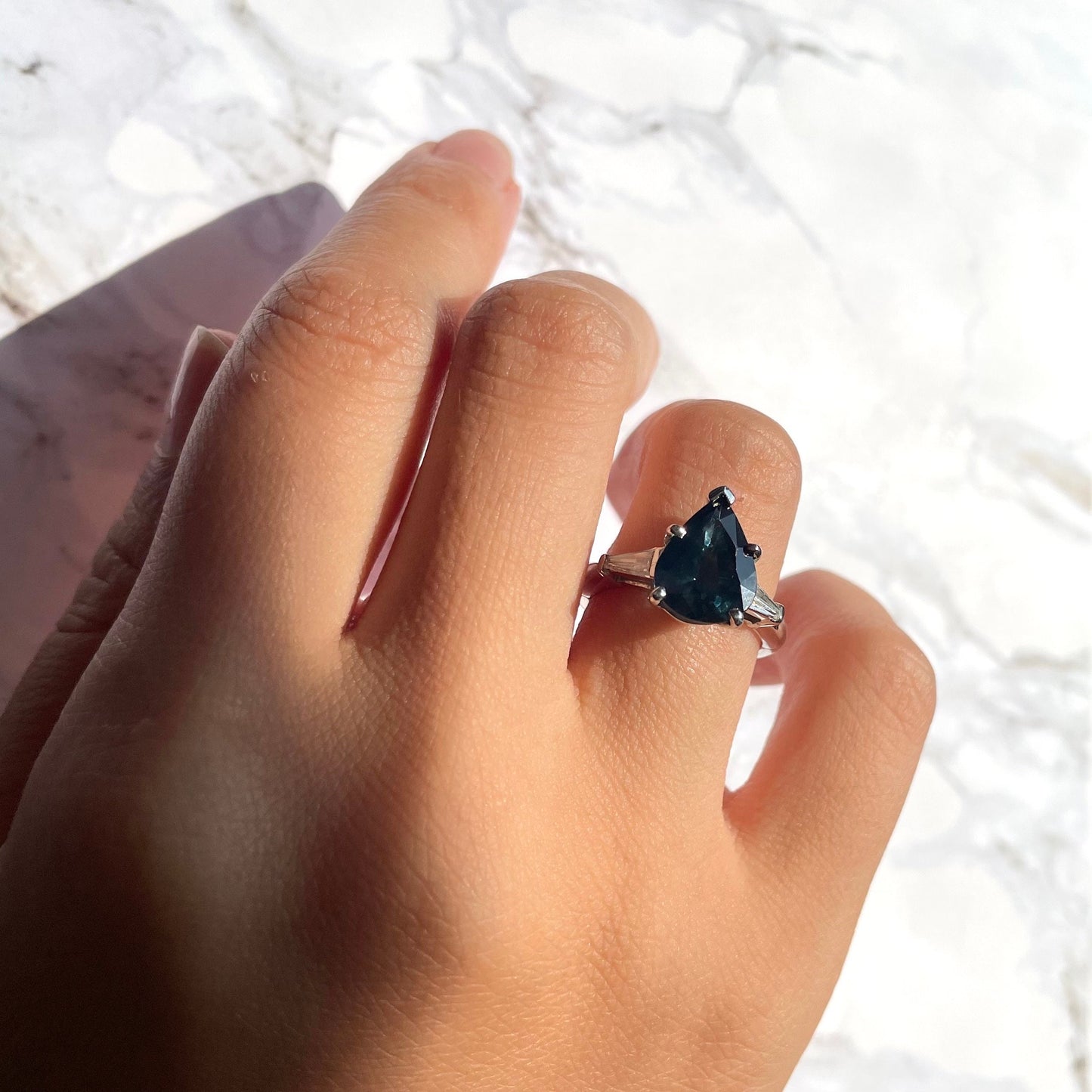 a hand wearing deep blue sapphire ring with 14k white gold band and natural white diamonds